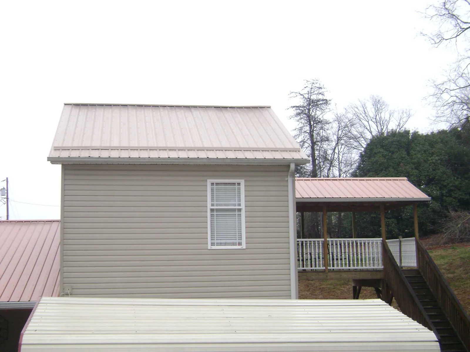 Tan metal roofs on a two story addition and attached porch, from a Roof Replacement job in Buffalo
